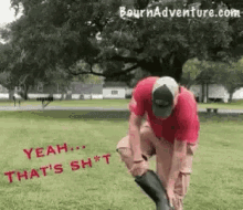 a man wearing a red shirt and a hat is putting on a pair of rubber boots in a park .