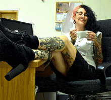 a woman with tattoos on her legs is sitting in a chair holding a cup