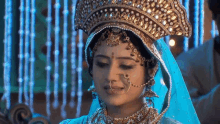 a woman wearing a crown and a nose ring is standing in front of a blue background .