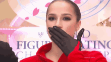 a woman in a red jacket is covering her mouth with her hand in front of a sign that says figure skating