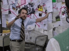 a man in a blue shirt and tie is pointing at a bulletin board covered in papers