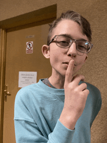 a boy wearing glasses holds his finger to his mouth