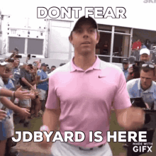 a man in a pink shirt is standing in front of a crowd of people and says `` dont fear jdbyard is here ''