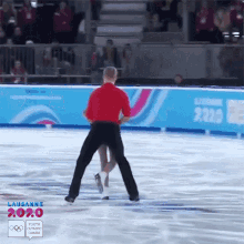 a man in a red shirt is holding a woman on a ice rink that says lausanne 2020 on it