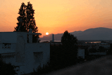 a sunset over a city with the sun setting behind a white building