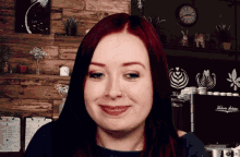 a woman with red hair is smiling in front of a wall with a clock and a sign that says victoria anderson