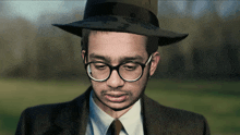 a man wearing a hat and glasses looks down at something