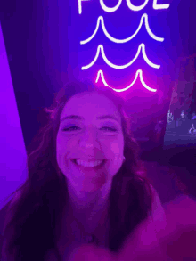 a woman is smiling in front of a purple neon sign that says pool