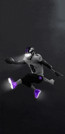 a football player wearing purple shoes and a helmet is jumping in the air with a football .