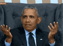 a man in a suit and tie is sitting in a chair with his hands up in front of a sign that says seburg