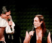 a man with long hair is holding a microphone and talking to another man with a beard .