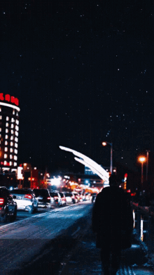 a person walking down a street at night with a large building in the background that says ' a ' on it