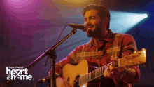 a man singing into a microphone while holding a guitar in front of a sign that says " heart & home "