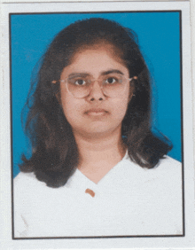 a woman wearing glasses and a white shirt stands in front of a blue backdrop