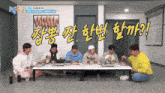 a group of men are sitting around a table eating food in a room with chinese writing on the wall behind them