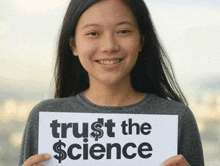 a young woman holds up a sign that says trust the science