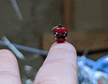 a small red apple with a green stem is on a finger