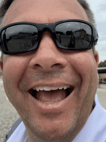 a man wearing sunglasses is smiling with a woman in sunglasses behind him