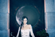 a woman in a white dress stands in front of a circle with the moon in the background