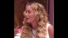 a woman with long blonde curly hair is sitting in front of a mirror with her eyes closed .