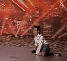 a young boy is kneeling on the floor in front of a stage with red lights .