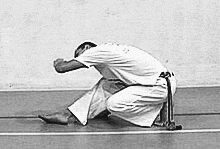 a black and white photo of a man kneeling on the floor with his head down .