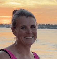 a woman in a pink tank top is smiling in front of the ocean