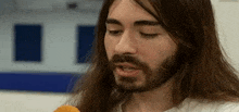 a man with long hair and a beard is eating a fried food .