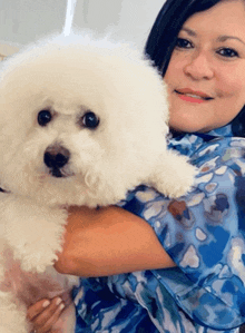 a woman in a blue shirt is holding a white dog