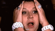 a woman with a surprised look on her face is holding her head with her hands .