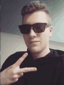 a man wearing sunglasses and a black shirt giving a peace sign