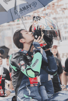 a man wearing a green yamaha jacket kisses his helmet