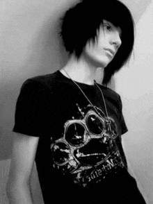 a young boy with long black hair is wearing a black t-shirt with a skull on it and a necklace .