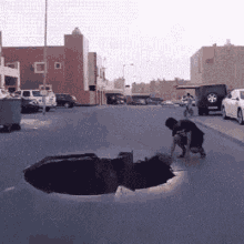 a man is kneeling down in front of a large hole in the ground on the side of the road .