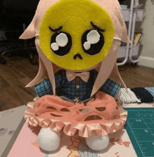 a stuffed doll with a yellow smiley face on her face is sitting on a table .