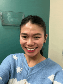 a smiling woman wearing a blue sweater with white clouds on it