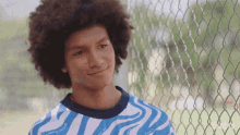 a young man wearing a blue and white zebra print shirt stands in front of a chain link fence and smiles for the camera