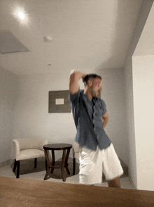 a man in a blue shirt and white shorts dances in a living room