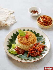 a plate of food with rice and vegetables on a leaf with a bowl of food in the background .