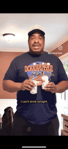 a man in a doghouse shirt holds two cans of beer