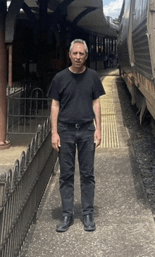 a man in a black shirt and black jeans is standing in front of a train