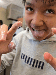 a young boy wearing a grey puma sweatshirt with his tongue out