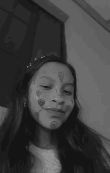 a black and white photo of a young girl with smiley faces painted on her face .