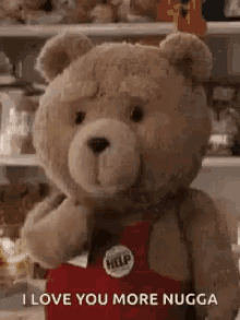 a teddy bear is wearing a red apron and saying `` i love you more nugga '' in front of a refrigerator .