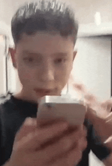 a young boy is holding a cell phone in his hands and making a funny face .