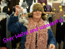 a woman wearing a fur hat and a pink scarf with the words stay weird and wonderful on the bottom