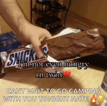 a person holding a snickers bar that says ' cant wait to go camping with you tonight nate '
