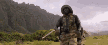 a man in a military uniform is standing in a field with mountains in the background holding a sword .