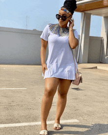 a woman in a white dress is standing in a parking lot talking on a cell phone