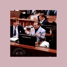 a man in a suit and tie is sitting at a desk with a computer monitor in front of him